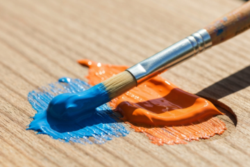 Dwa pędzle skrzyżowane na drewnianej palecie z niebieską i pomarańczową farbą